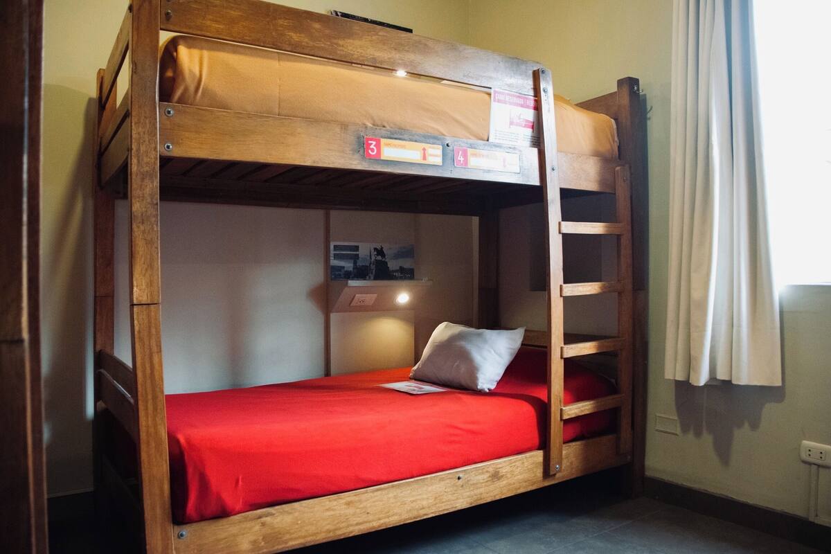 A bunk bed with a red mattress and a pillow, a wooden ladder, and a small shelf with a poster.
