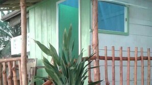 A small, single-story building with a green door and a window. There is a staircase leading to a porch with a wooden railing. A potted plant is in front of the building. - Luna Beach Home & Cabanas - Hostel (Boossa)