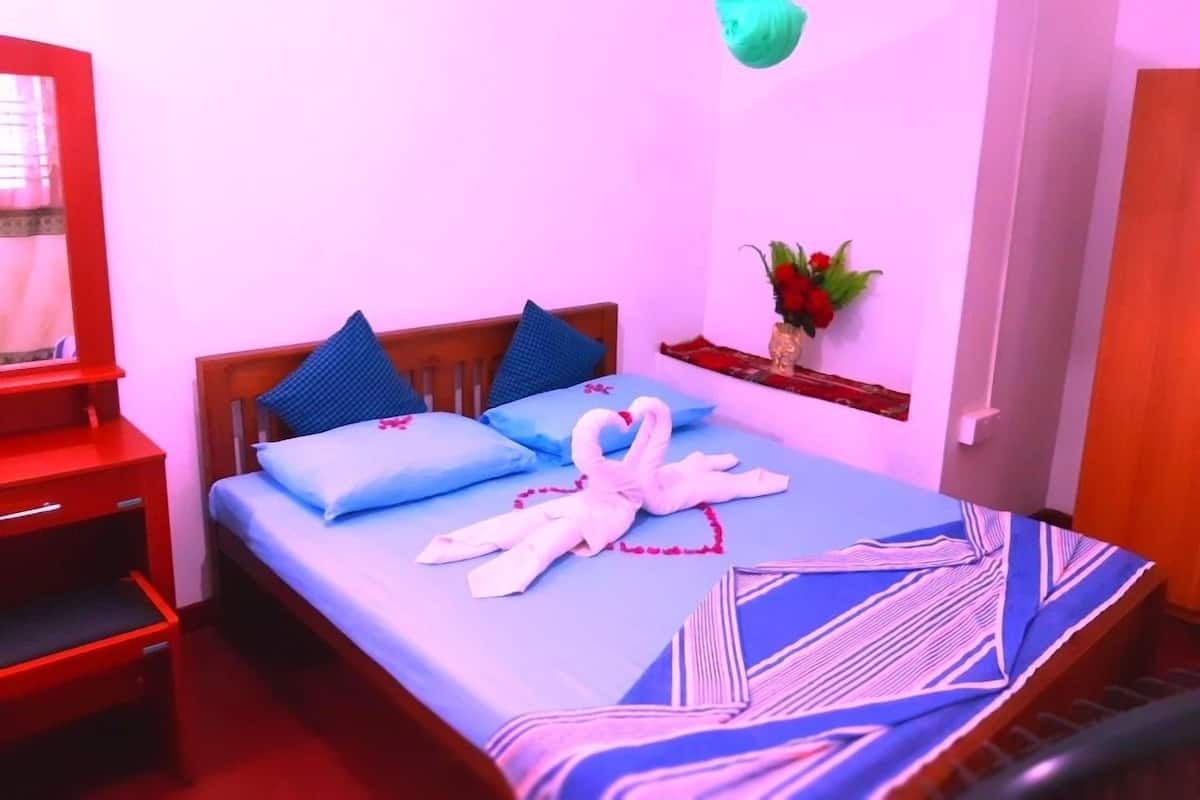 A bedroom with a bed, pillows, a bedside table, a mirror, a vase with flowers, and a hanging decoration.