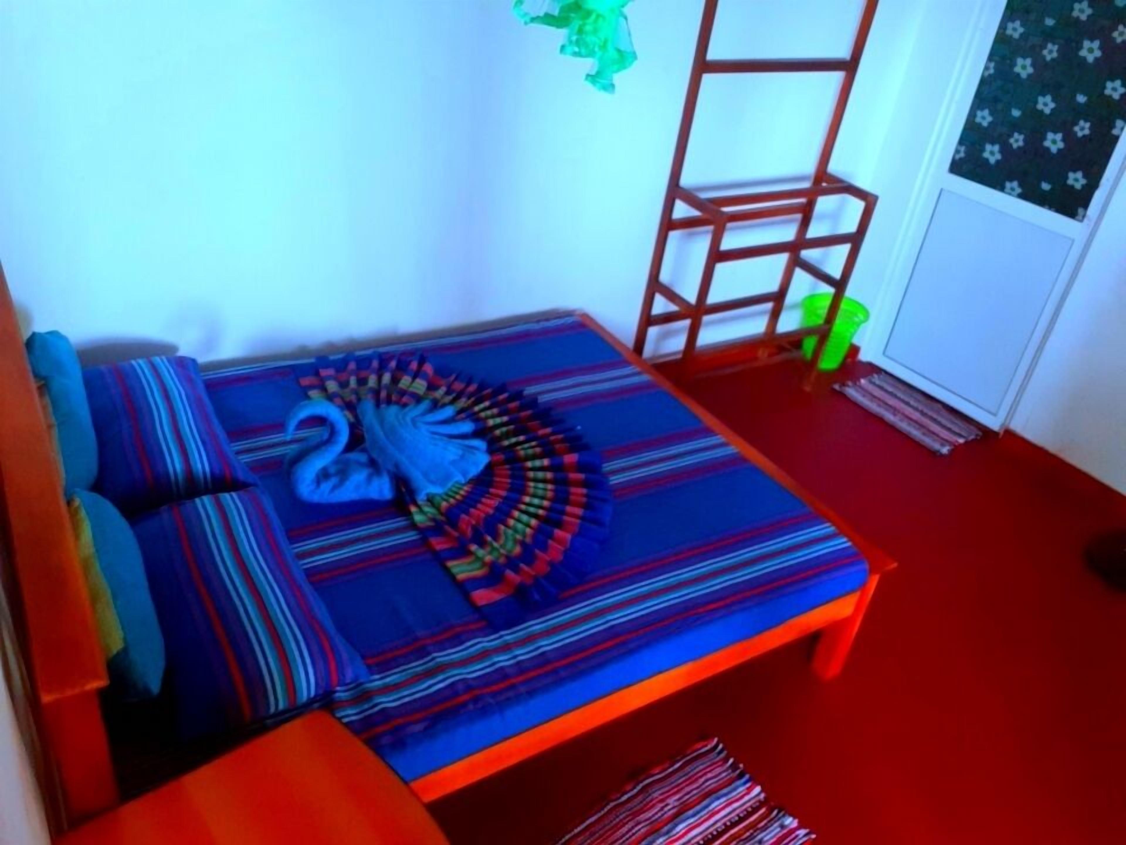 A small, cozy room with a bed, a wooden ladder, and a window with a patterned curtain.
