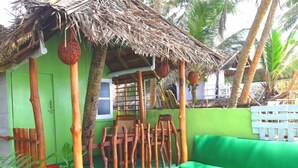 A small, green-roofed structure with a thatched roof, wooden chairs, and a green sofa. - Luna Beach Home & Cabanas - Hostel (Boossa)