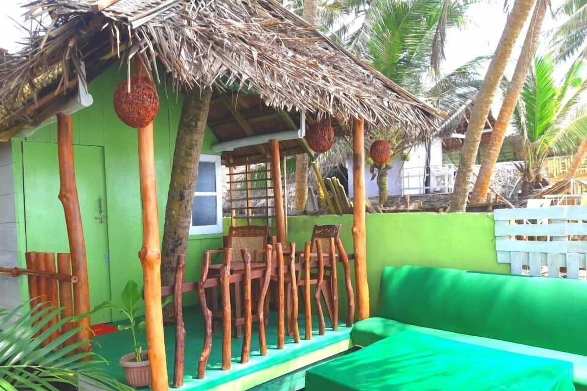 A small, green-roofed structure with a thatched roof, wooden chairs, and a green sofa.