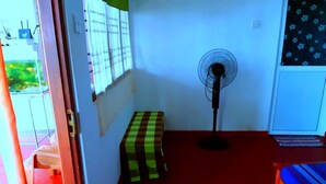 A small room with a checkered bench, a standing fan, and a window with blinds. - Luna Beach Home & Cabanas - Hostel (Boossa)