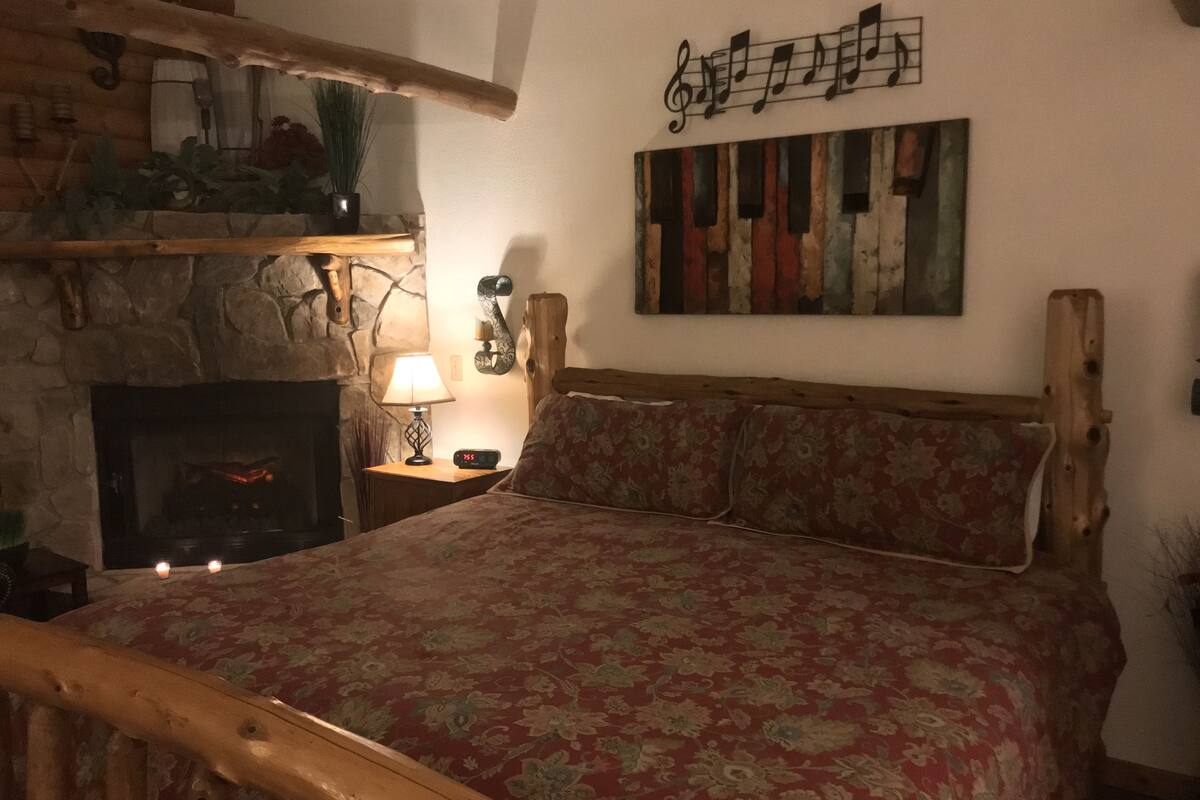 A cozy room with a bed, a fireplace, a clock, and a wall with a musical note decoration.