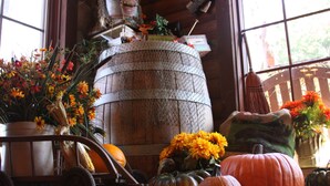 Ein rustikales Interieur mit einem Holzfass, Kürbissen und verschiedenen Blumen.