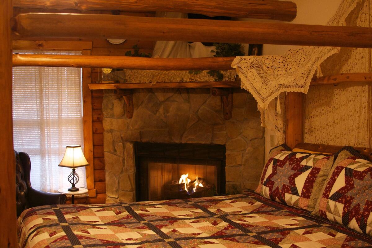 A cozy room with a stone fireplace, a quilted bedspread, and a wooden ceiling.