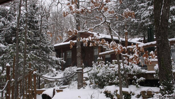 Eine Holzblockhütte, umgeben von schneebedeckten Bäumen und einer Holzterrasse.