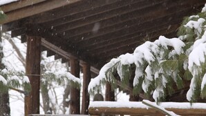 Eine hölzerne Veranda mit schneebedeckten Tannenzweigen.