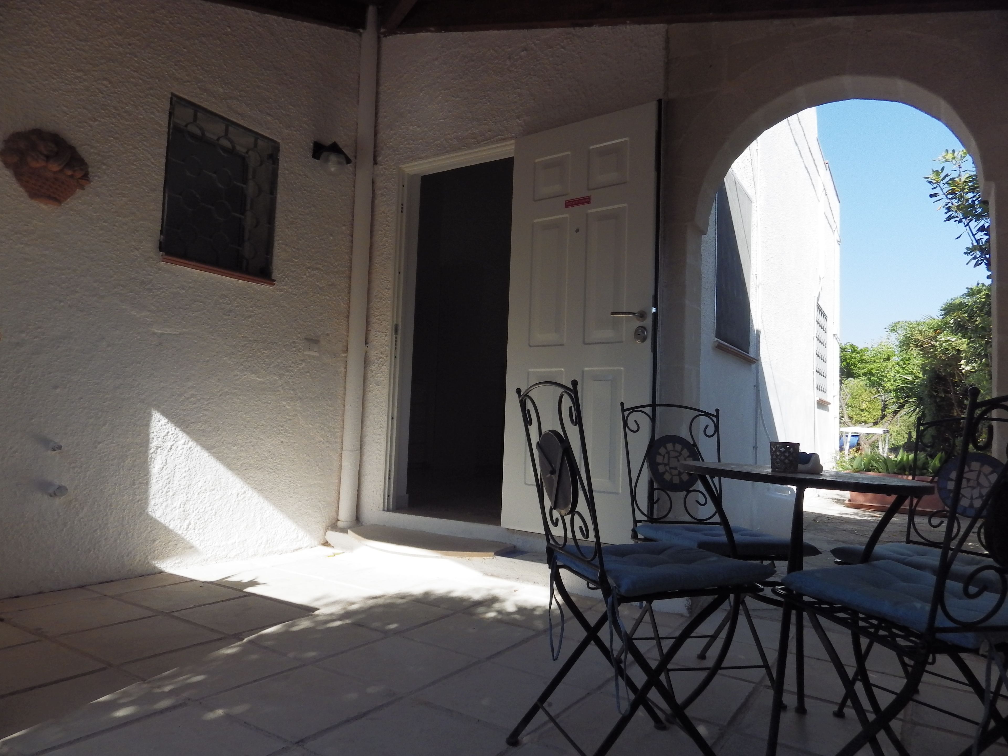 A covered patio area with a white wall, a door, and a small table with chairs.