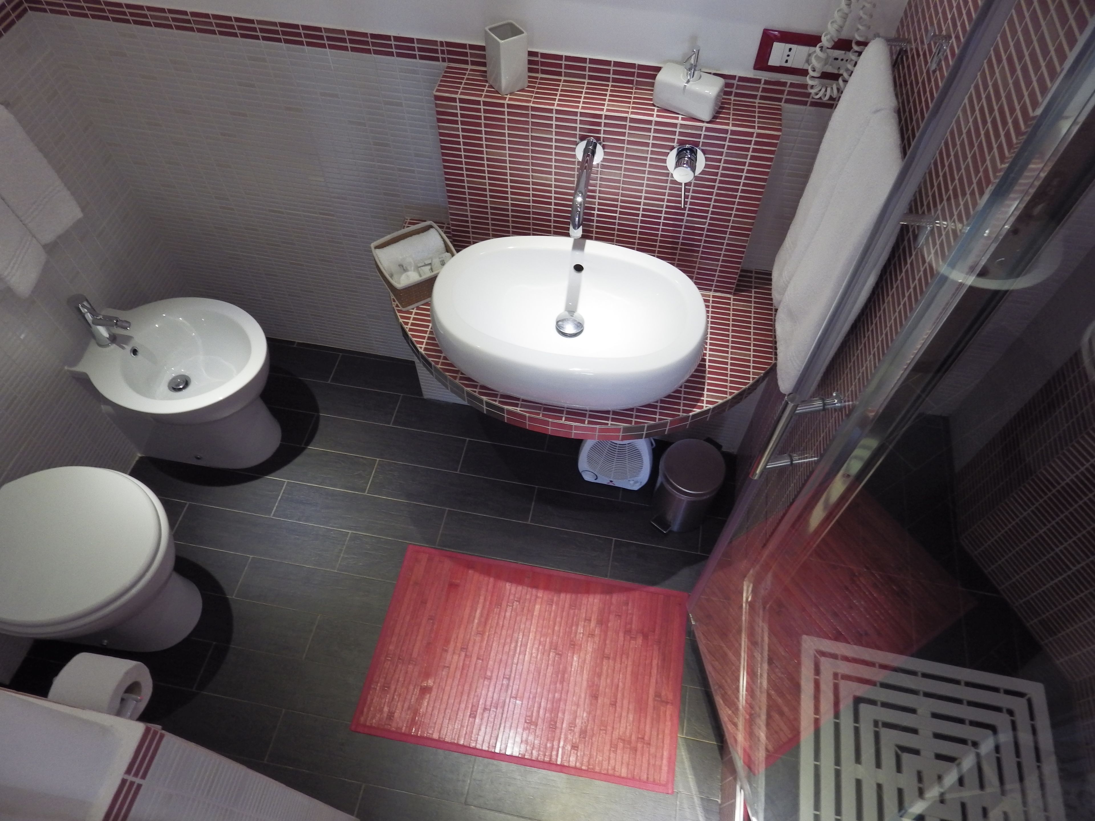 A compact bathroom with a white sink, a white toilet, and a bidet.