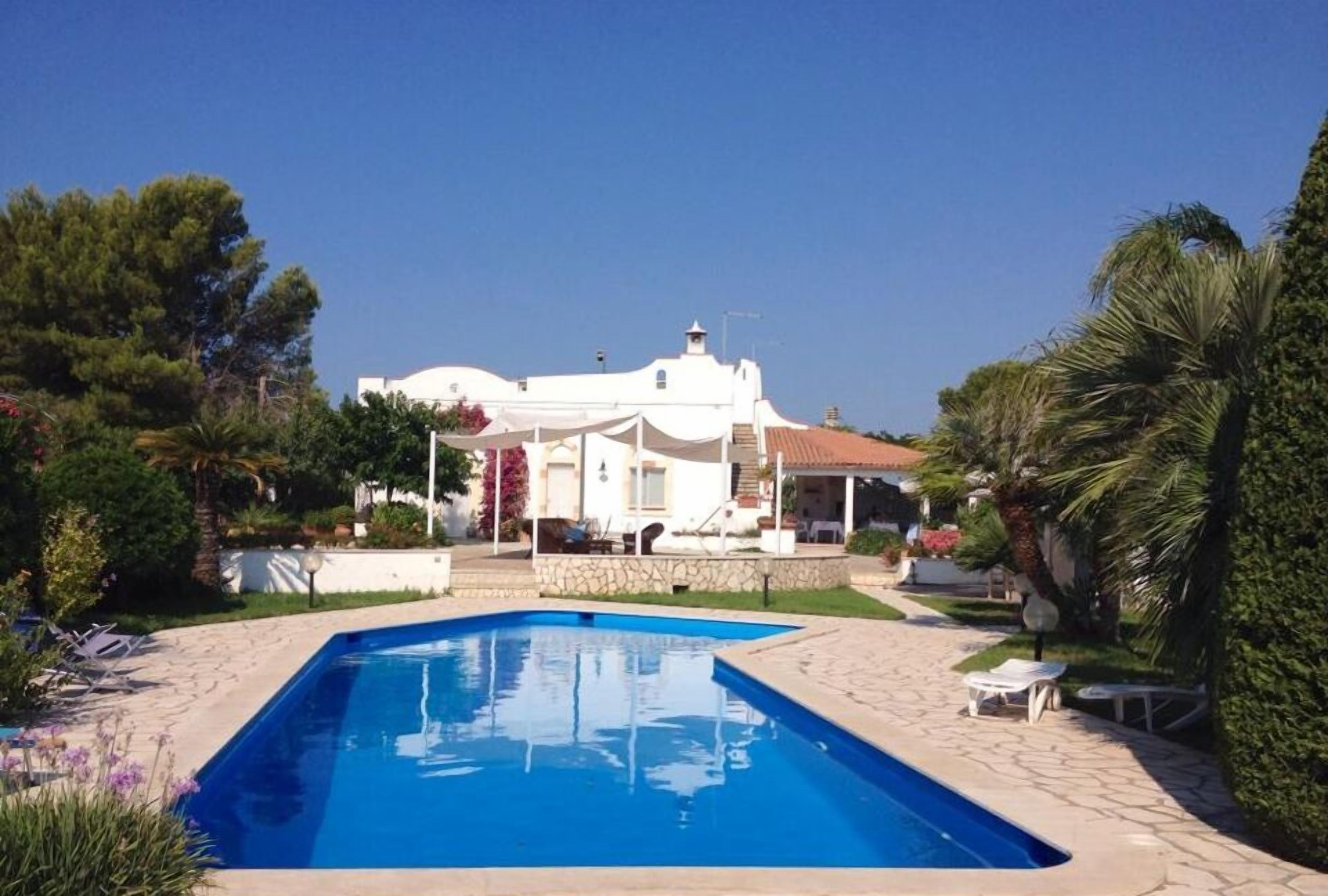 A poolside view of a white villa with a stone pathway leading to a covered patio area.