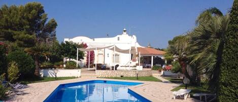 A poolside view of a white villa with a stone pathway leading to a covered patio area.