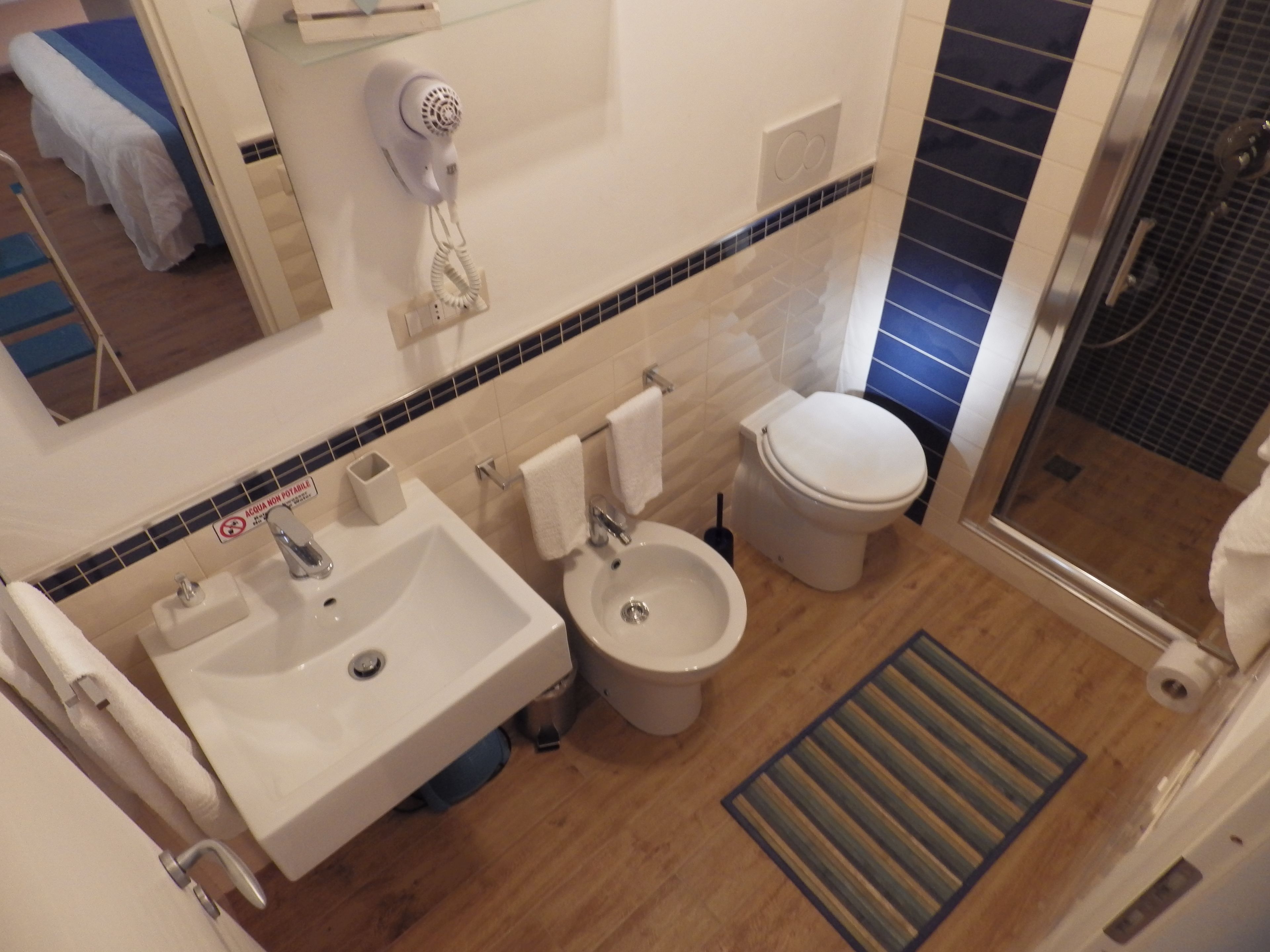 A bathroom with a sink, bidet, toilet, and a hairdryer mounted on the wall.