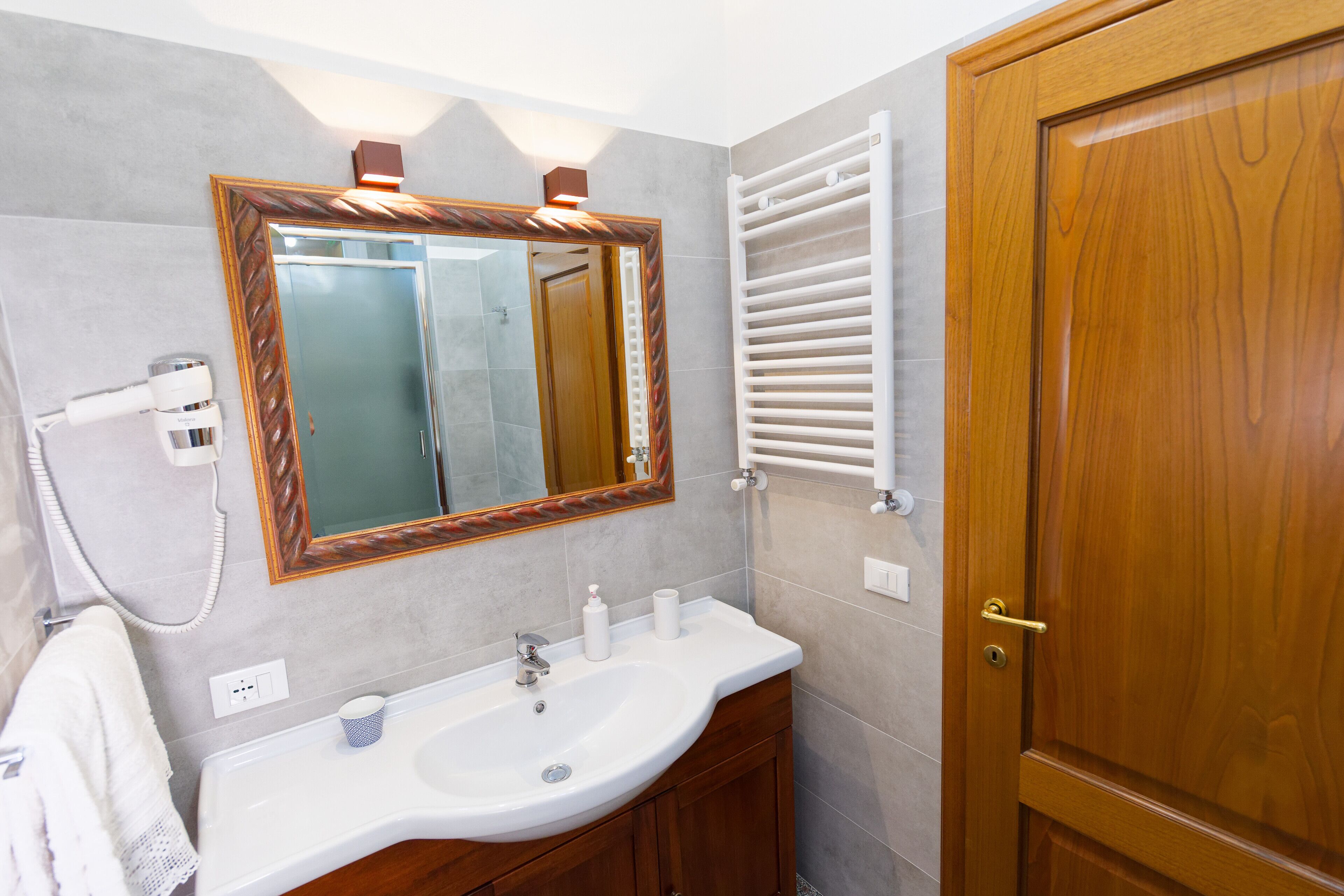 Un baño con un lavamanos blanco, tocador de madera, un espejo con marco de madera, un perchero para toallas y una puerta de madera.