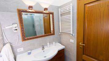 Un baño con un lavamanos blanco, tocador de madera, un espejo con marco de madera, un perchero para toallas y una puerta de madera.