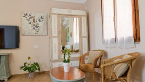 Un salon avec un téléviseur, une plante en pot, des fauteuils en osier et un miroir.