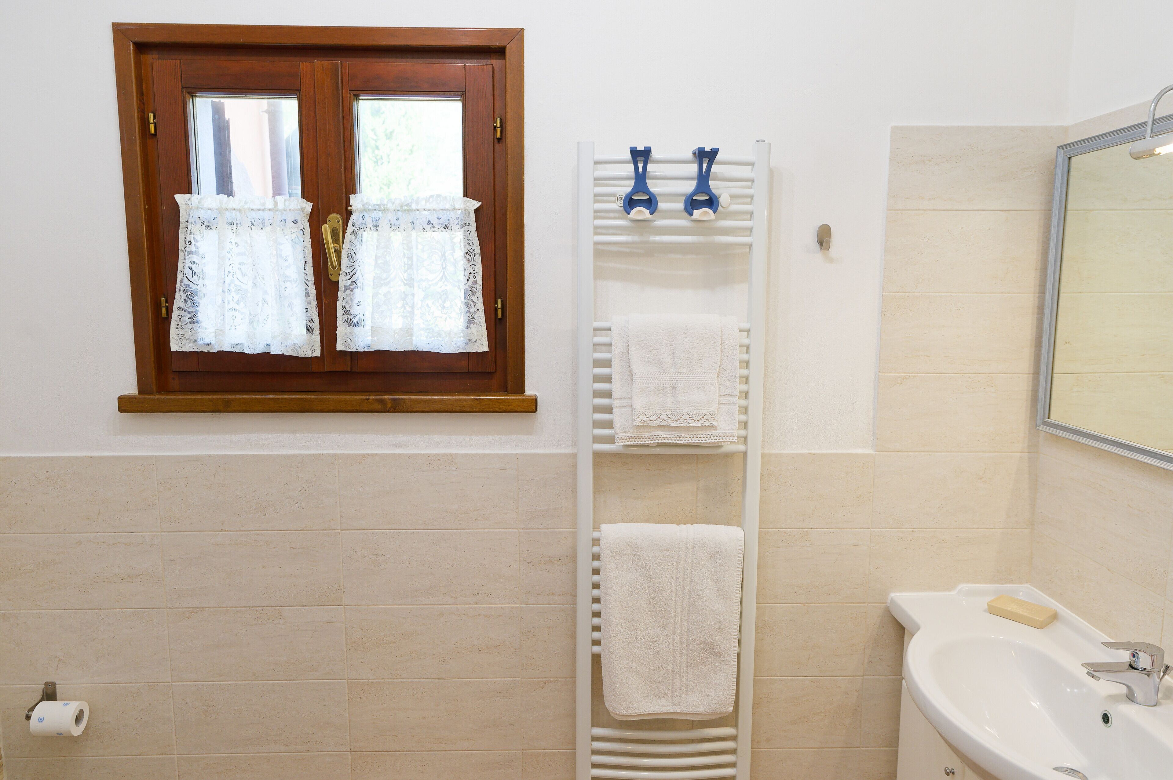 Un baño con ventana de madera, un perchero, un lavabo y un espejo.