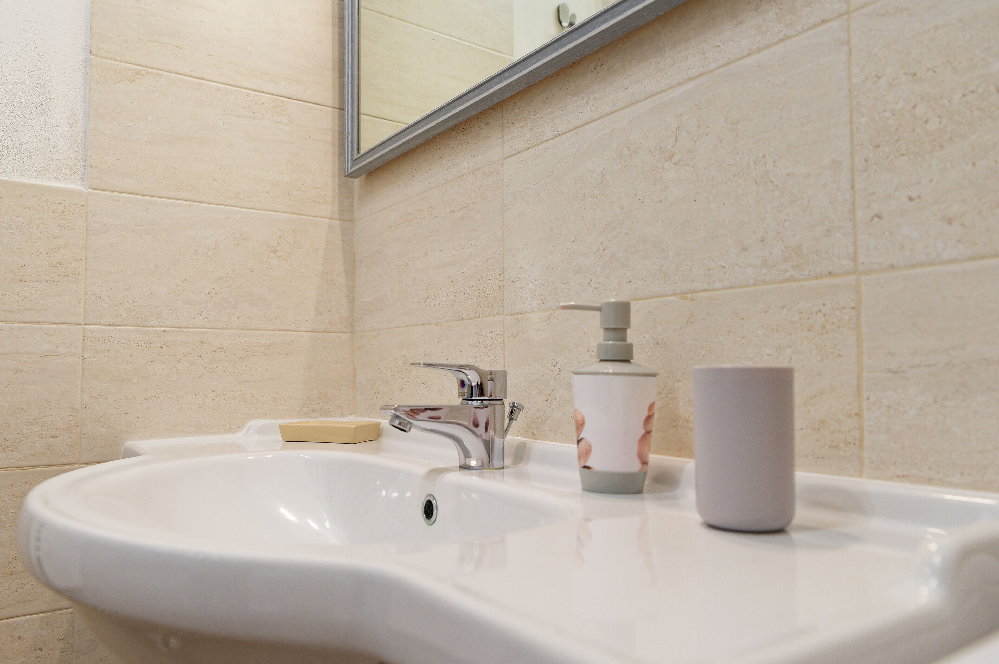 A bathroom with a white sink, a soap dispenser, and a cup on the counter.