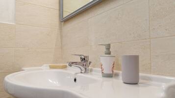A bathroom with a white sink, a soap dispenser, and a cup on the counter.
