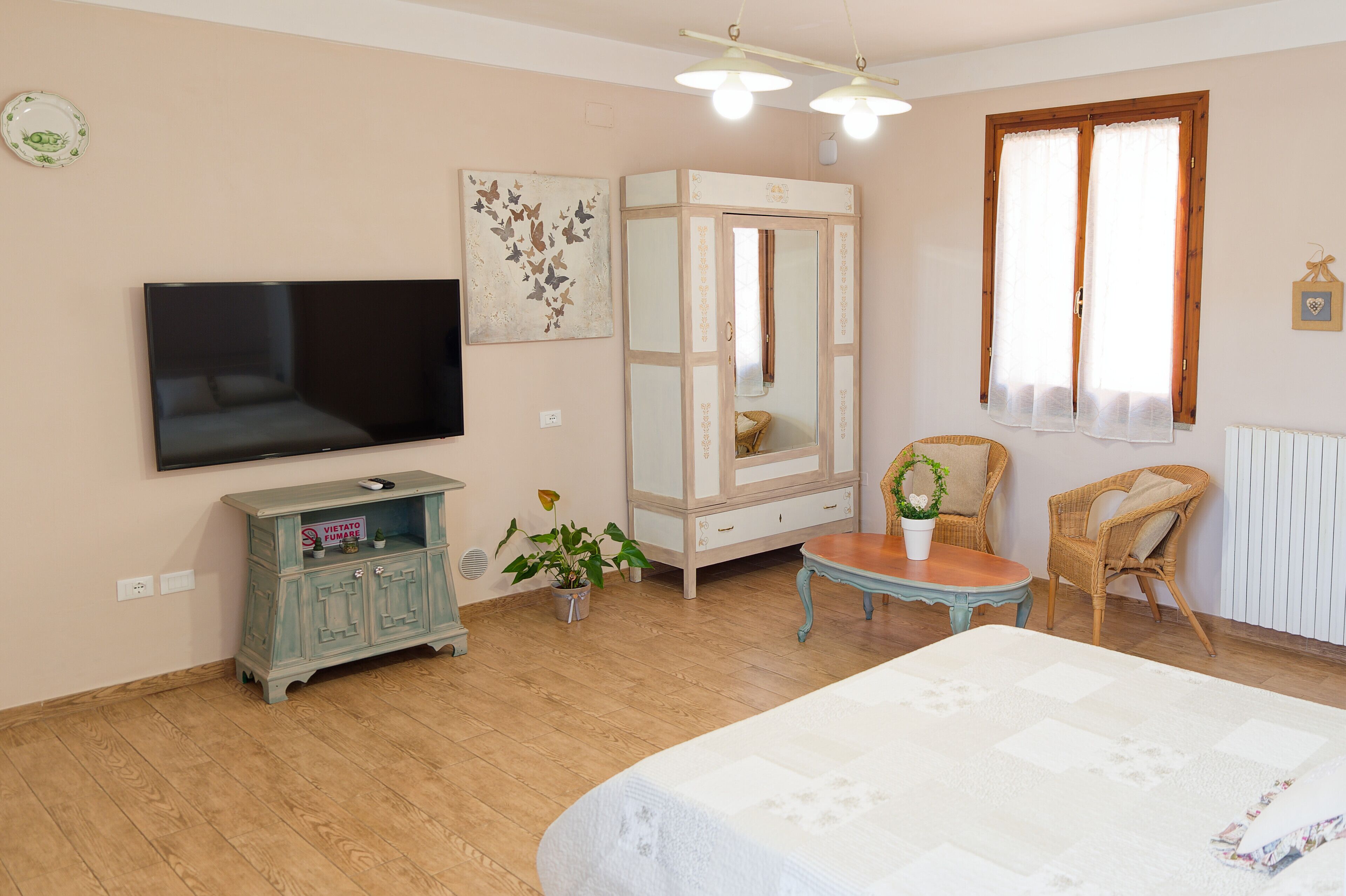 A bedroom with a bed, a television, a wardrobe, a chair, and a small table with a plant.