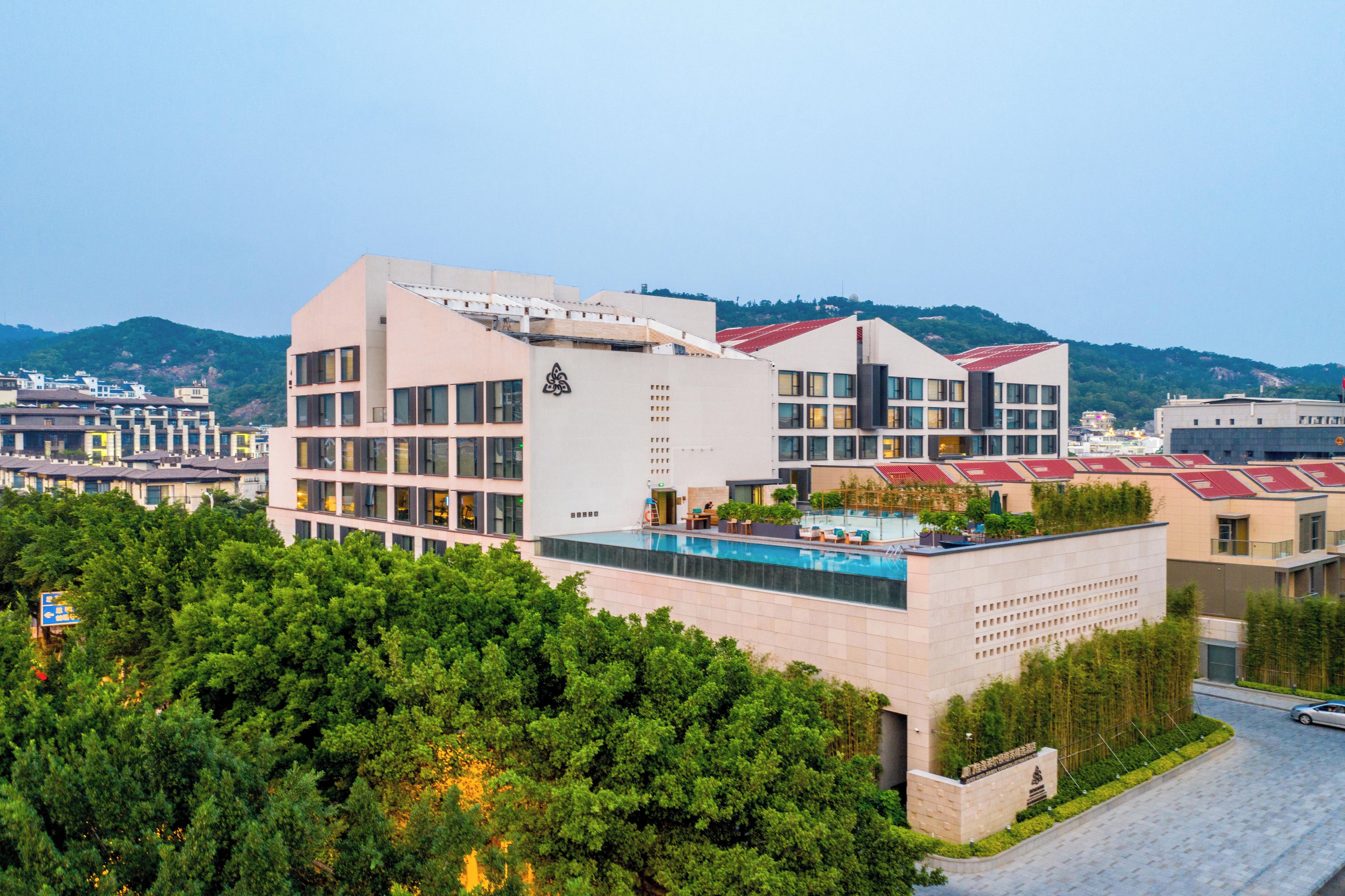 Un edificio moderno con piscina, rodeado de vegetación y colinas al fondo.