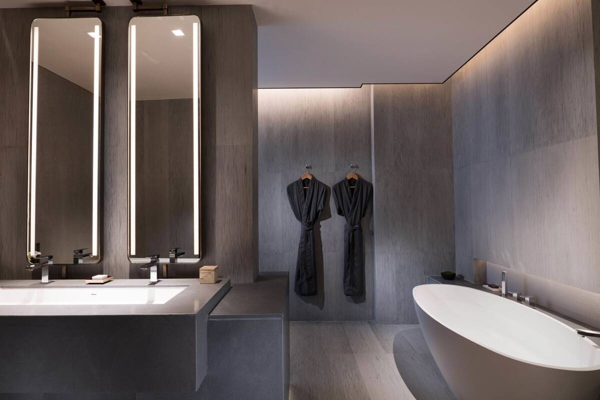 Une salle de bain moderne avec un grand miroir, une baignoire et deux peignoirs accrochés au mur.