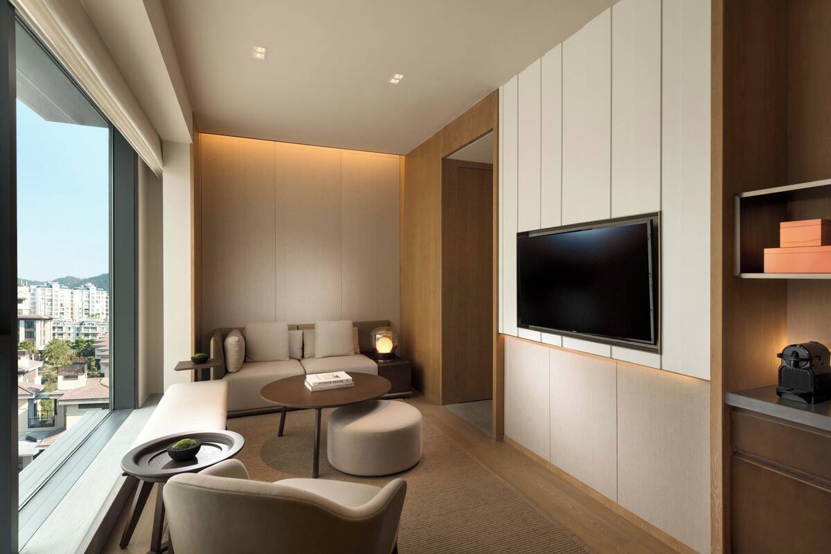 Une chambre d’hôtel moderne dotée d’une grande télévision, de sièges confortables, d’une petite table et offrant une vue sur la ville.