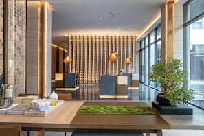 Um lobby moderno de hotel com balcão de recepção, área de estar e uma grande janela.