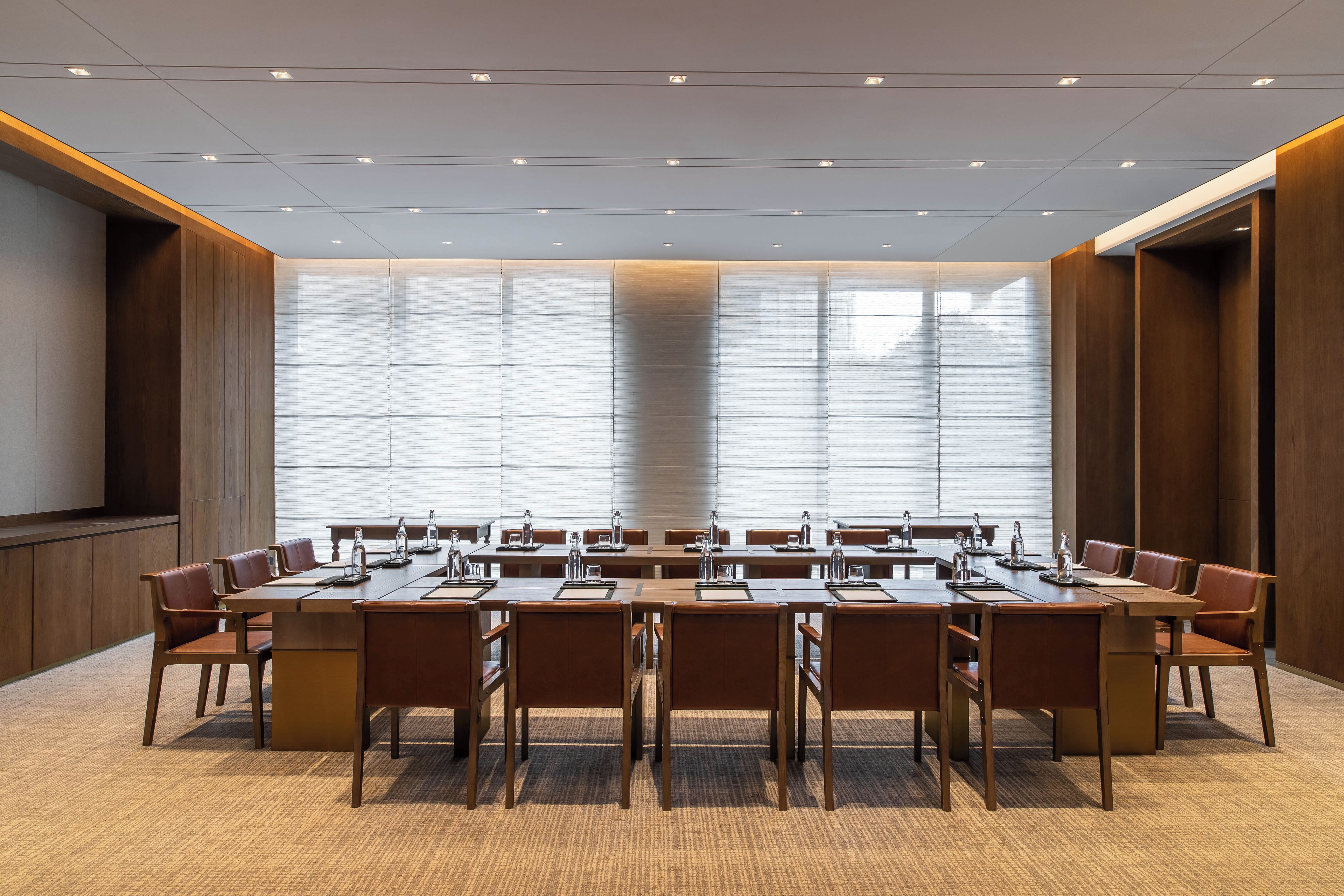 Une salle de conférence avec une longue table, de nombreuses chaises et une grande fenêtre équipée de stores.