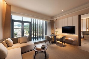 Une chambre d’hôtel moderne dotée d’une grande fenêtre, d’un canapé, d’une table à manger, d’un téléviseur et d’une petite table d’appoint.