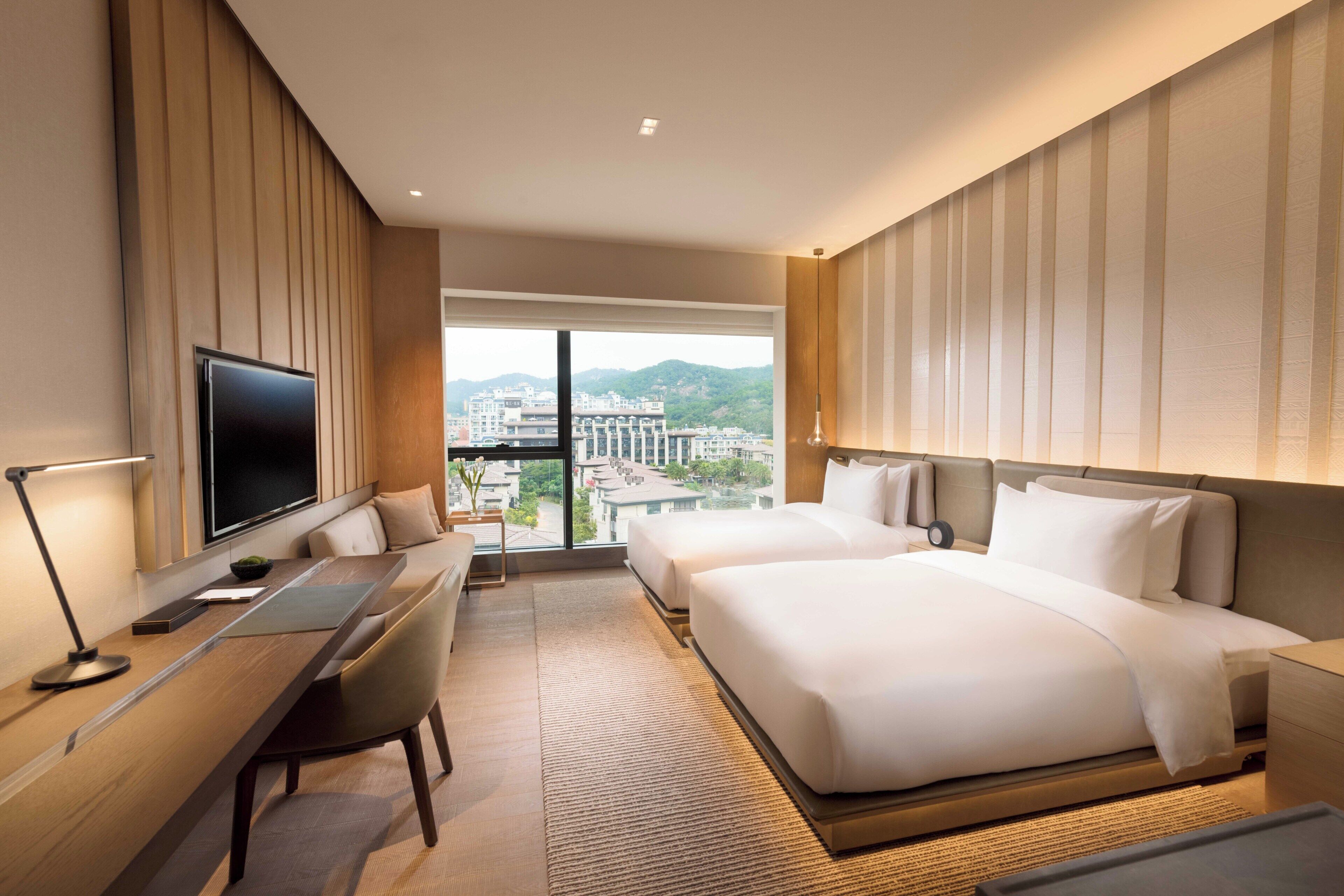 Habitación de hotel con una cama grande, un escritorio con computadora, un televisor y vista a la ciudad.