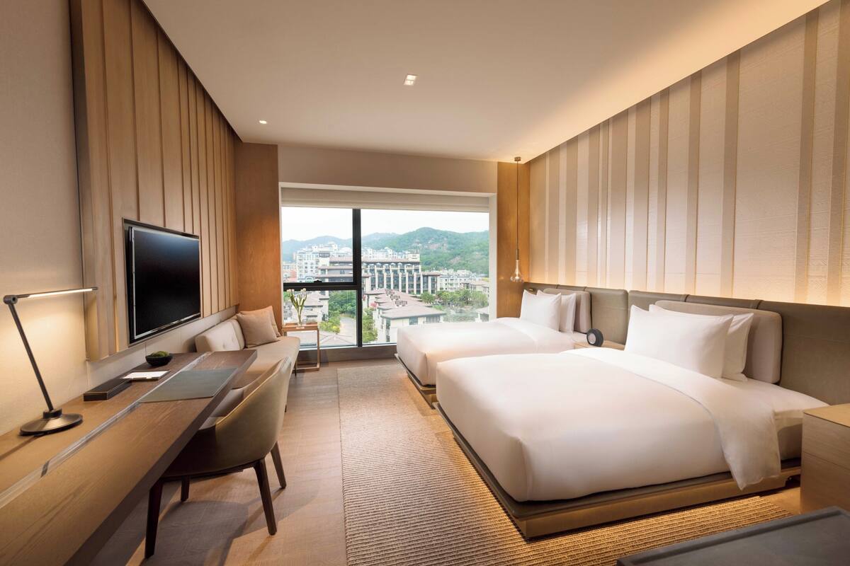 Une chambre d’hôtel avec un grand lit, un bureau avec un ordinateur, une télévision et une vue sur le paysage urbain.