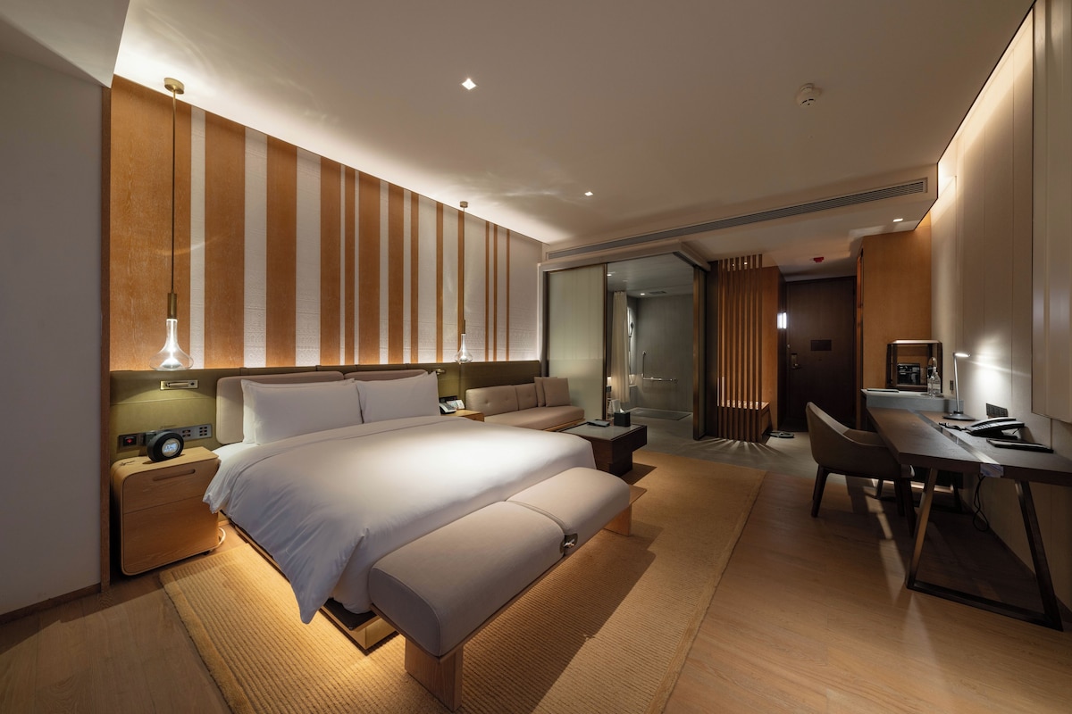 Quarto de hotel moderno com uma cama grande, uma mesa de trabalho e um espaço de estar.