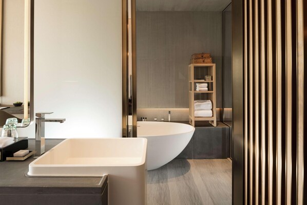 A modern bathroom with a freestanding bathtub, a vanity with a mirror, and a shelf with towels. - Joyze Hotel Xiamen Curio Collection by Hilton (Xiamen)