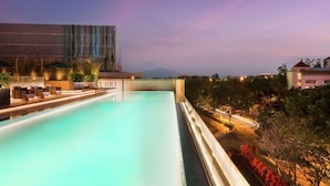 A swimming pool with lounge chairs and a view of a building with a modern design. - Joyze Hotel Xiamen Curio Collection by Hilton (Xiamen)