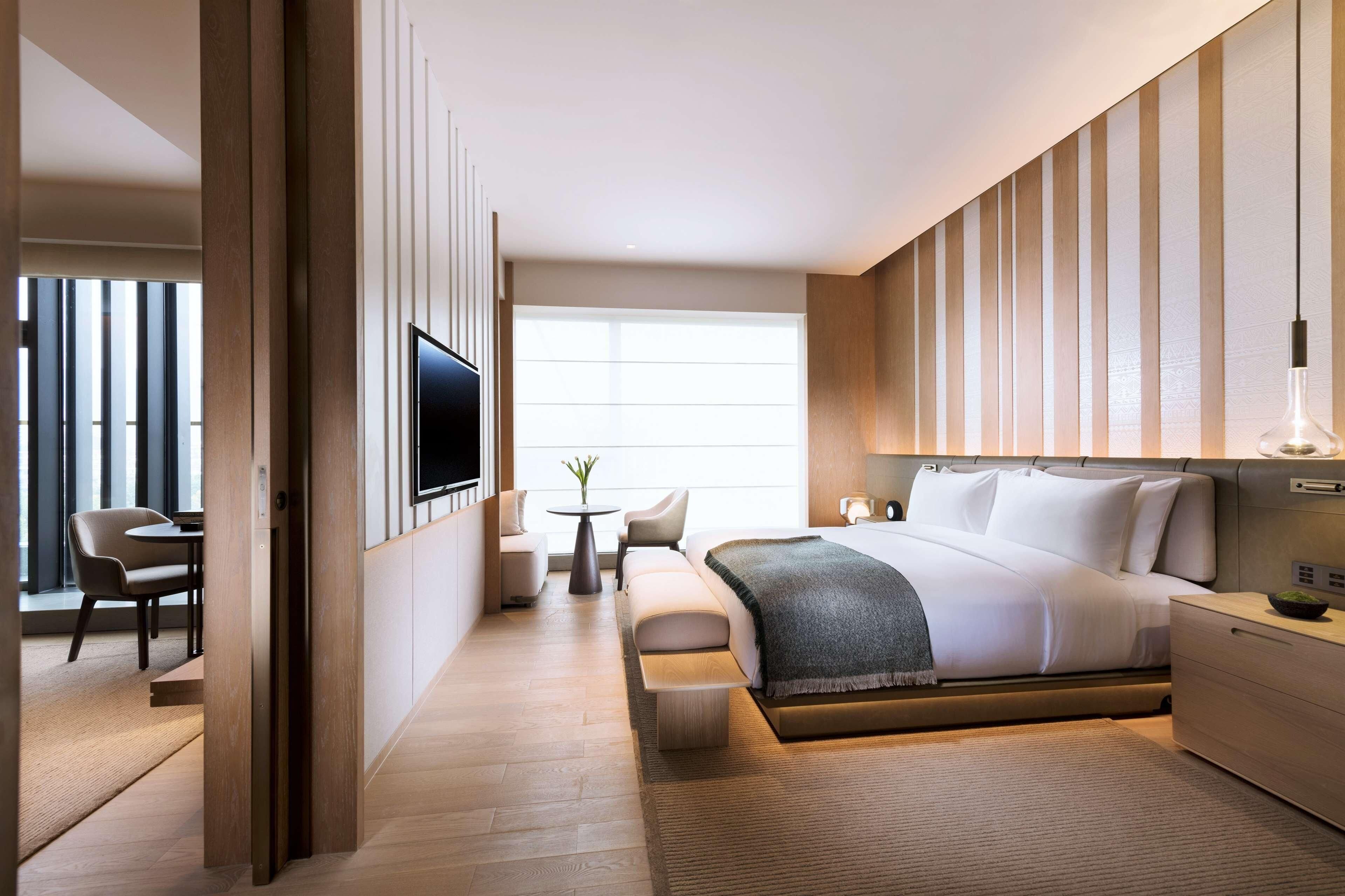 Quarto de hotel moderno com uma cama grande, uma escrivaninha, uma cadeira e uma televisão.