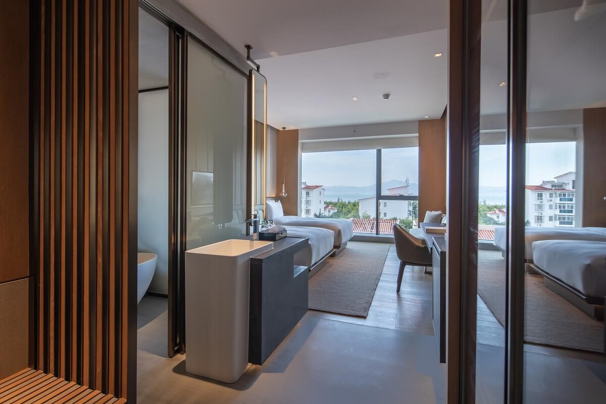 Quarto de hotel moderno com uma cama grande, uma mesa de trabalho e vista para a cidade.