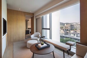 A modern living room with a large window, a sofa, a round table, and a flat-screen TV. - Joyze Hotel Xiamen Curio Collection by Hilton (Xiamen)