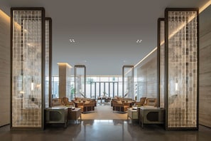 Um hall amplo com design moderno, destacando uma área de estar central com sofás e poltronas, janelas grandes e piso lustroso.