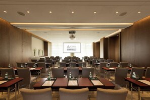 A conference room with multiple tables and chairs, a large screen at the front, and a sign indicating it's a 'CUB Collection by Hilton' room. - Joyze Hotel Xiamen Curio Collection by Hilton (Xiamen)