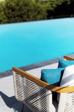 A wicker lounge chair with cushions by a pool. - Joyze Hotel Xiamen Curio Collection by Hilton (Xiamen)