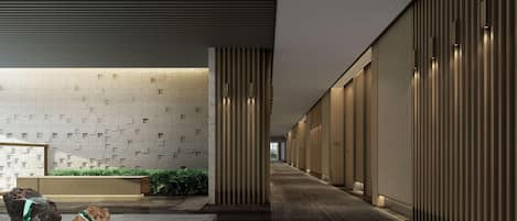A modern corridor with a patterned wall, a reception area with a reception desk, and a seating area with a small water feature.