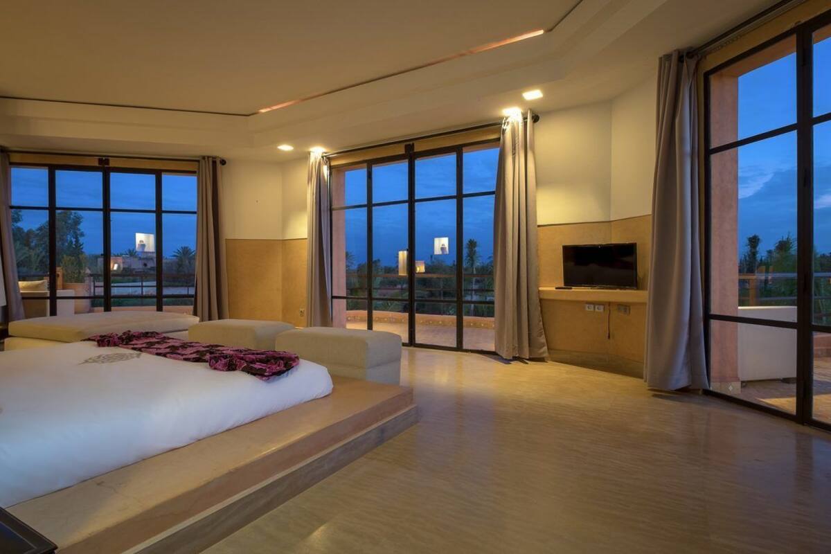A spacious bedroom with a large bed, a TV, and a balcony with a view.