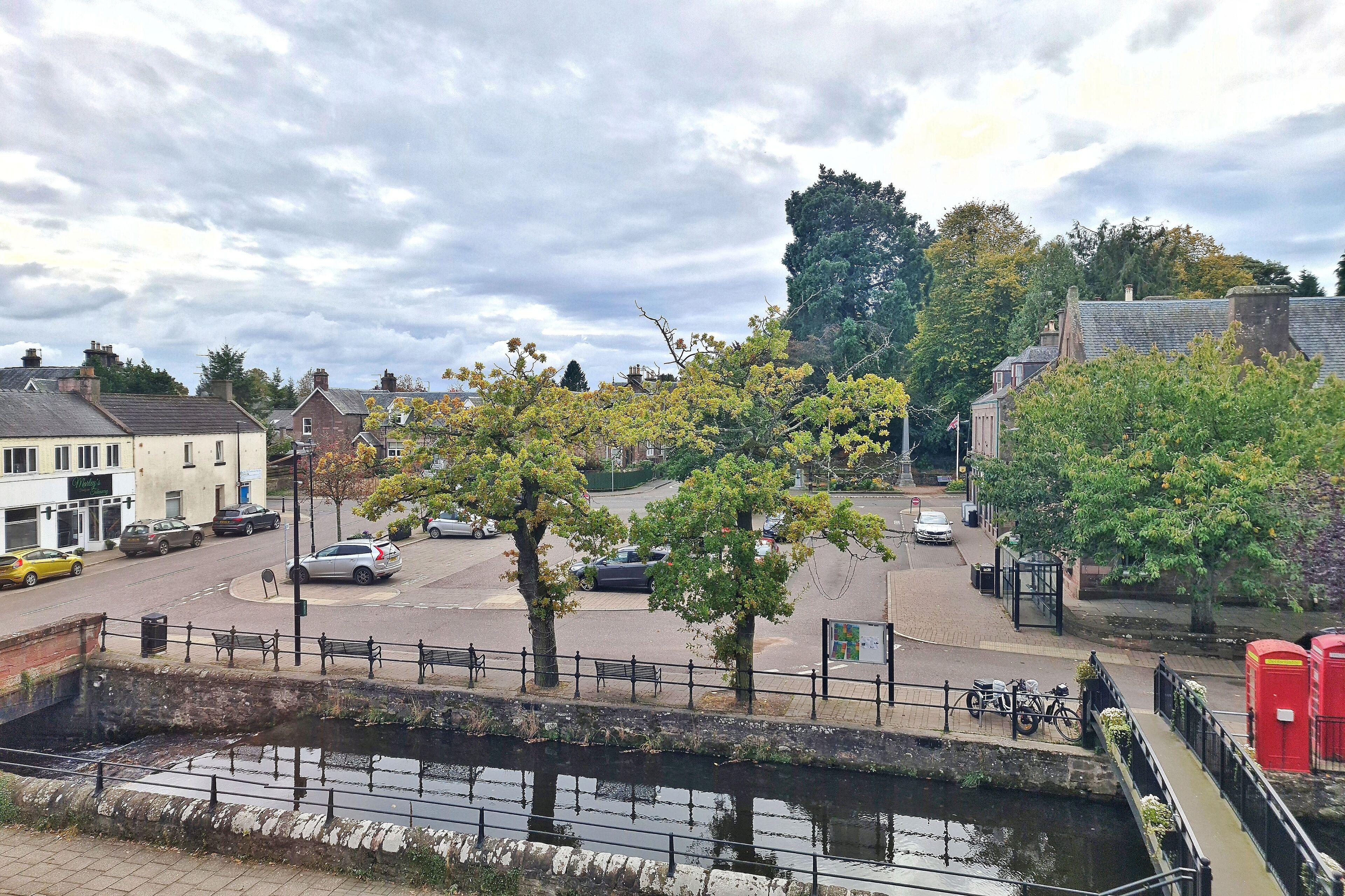 A riverside view with a bridge, trees, and buildings.