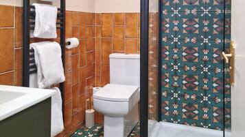 A bathroom with a toilet, a towel rack with white towels, a toilet paper holder, and a patterned tile floor.