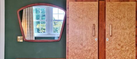 Une pièce avec un mur vert, une coiffeuse en bois, un miroir et une armoire en bois.