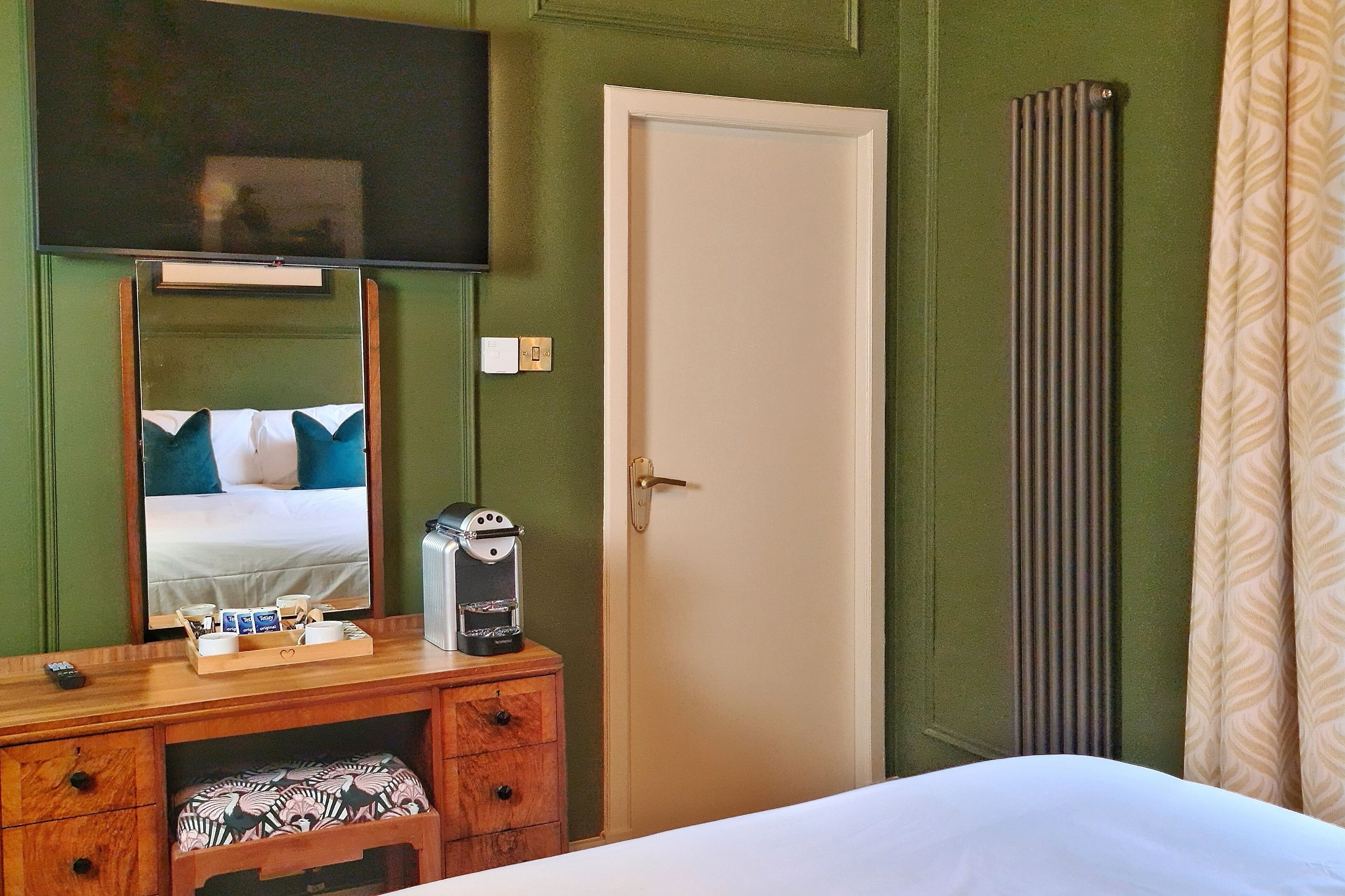 Une chambre d’hôtel comprenant un lit, une commode en bois avec un miroir, une machine à café et un téléviseur fixé au mur.