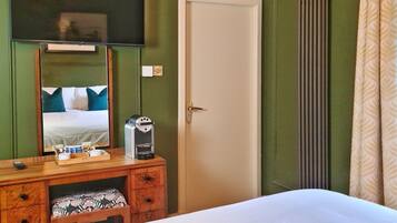Une chambre d’hôtel comprenant un lit, une commode en bois avec un miroir, une machine à café et un téléviseur fixé au mur.
