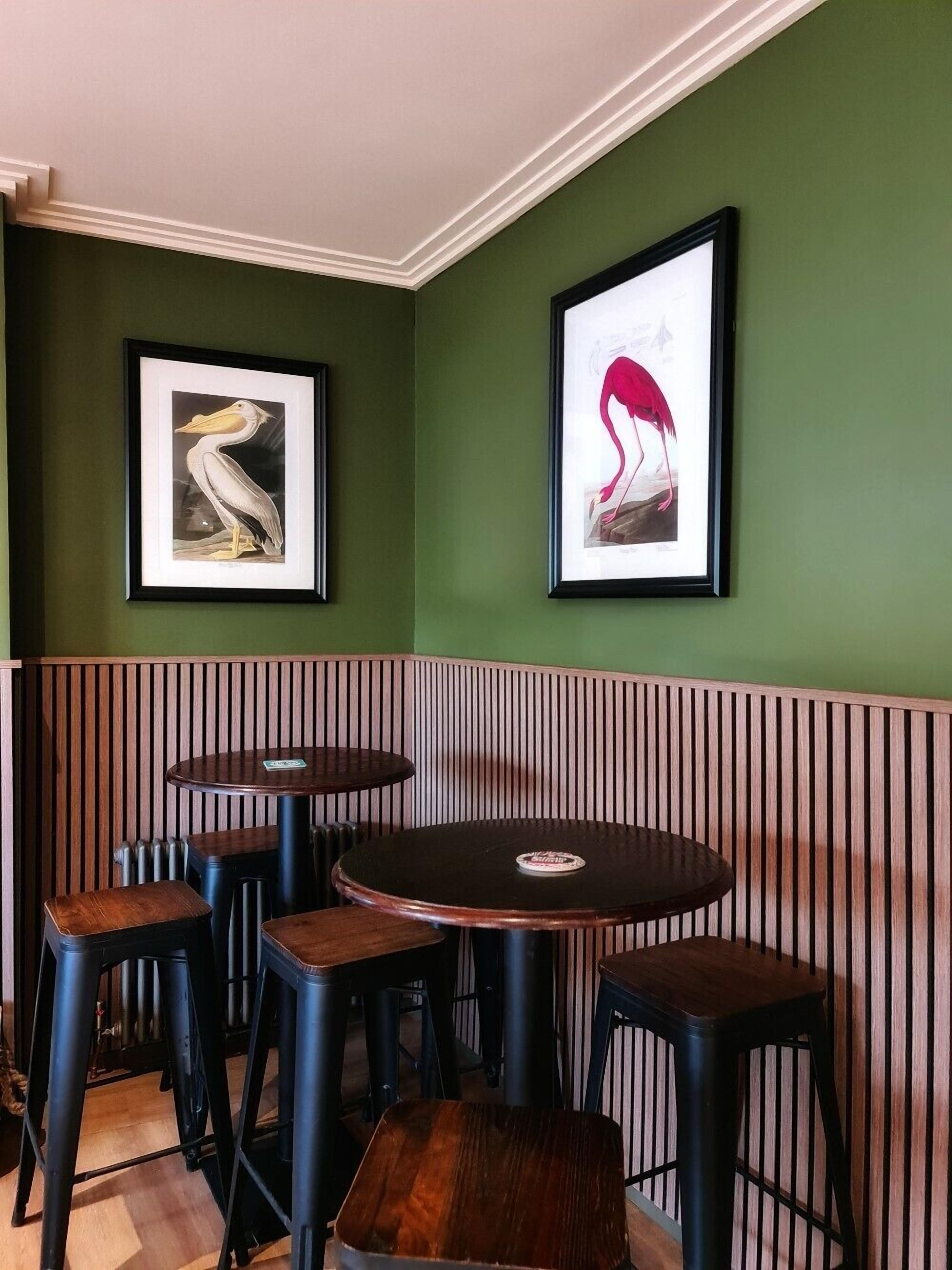 Un angolo di ristorante con pareti verdi, due opere d'arte incorniciate e una zona con banconi e sgabelli.
