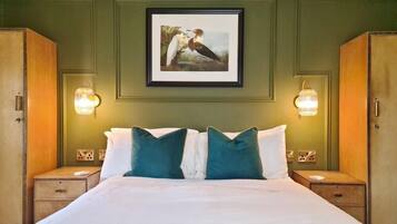 Habitación de hotel con cama, dos mesitas de noche, un cuadro enmarcado sobre la cama y lámparas fijadas a la pared.